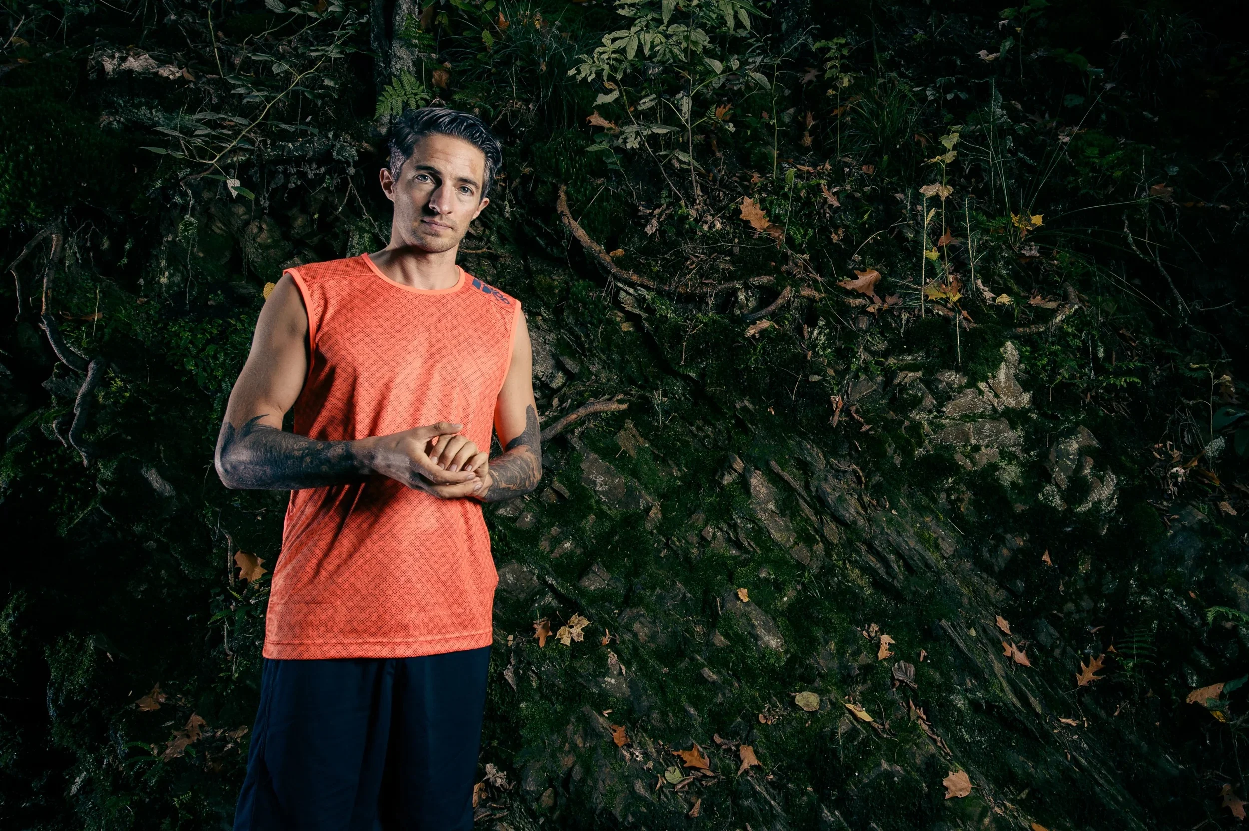 Studio portrait of a male runner in orange athletic wear against a dark background.